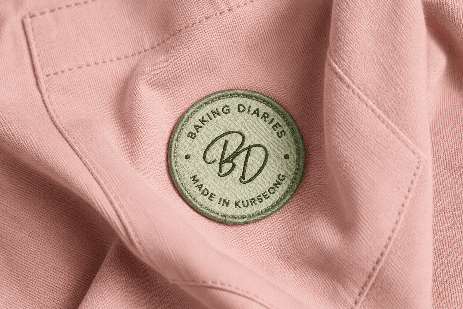 Baking Diaries monogram embroidered as a patch on a pink apron